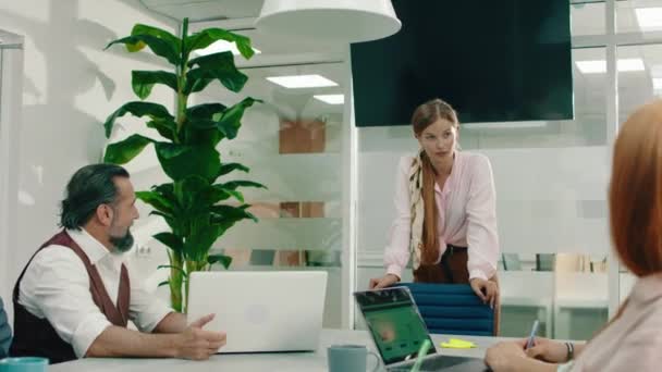 Una donna molto bella con lunghi capelli biondi legati alla schiena sta parlando con gli altri suoi colleghi mentre discute di questioni di lavoro in una stanza dell'ufficio molto luminosa e moderna. — Video Stock