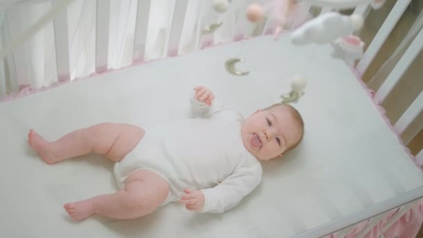 Incrível bonito bebê menina sozinha em seu berço brincando com as mãos e pernas e olhando para cima o conceito de brinquedos de berço de bebê e infância — Vídeo de Stock