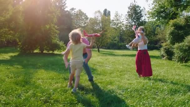 Una familia carismática con dos niños pequeños jugando en la naturaleza en la hierba que son muy felices — Vídeos de Stock