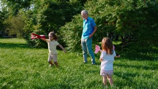 Charismatischer alter Mann und seine zwei Kinder spielen im Park mit dem Flugzeug und genießen die Zeit in der Natur — Stockvideo