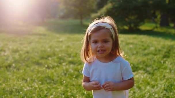 Sätta en söt liten flicka framför kameran i mitten av parken i en solig dag hon ler mycket söt — Stockvideo