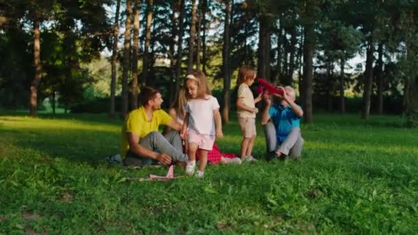 Leende stora glada föräldrar tillsammans med farfar leker med två söta små barn i flygplanet njuta av ögonblicket i parken — Stockvideo
