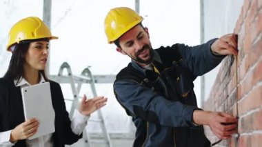 Kameranın önünde iyi görünümlü kadın yönetici ve inşaat alanında karizmatik işçi aynı anda hem duvardan bazı önlemler alıp hem de tartışmalar yapıyorlar.