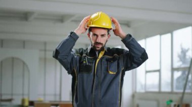 Büyük inşaat alanında iyi görünümlü bir adam kaskını çıkarır ve doğrudan kameraya bakar.