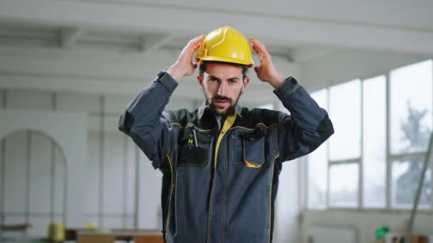 Auf Großbaustelle nimmt gut aussehender Mann seinen Schutzhelm ab und blickt konzentriert in die Kamera — Stockvideo