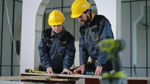 Feliz dois trabalhadores construtores mulher e homem com equipamentos de segurança e capacetes analisando o plano de construção sorridente grande — Vídeo de Stock