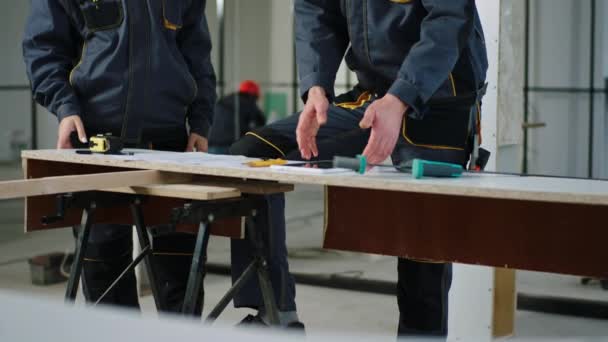 Chantier de construction moderne en face de la femme ingénieur de la caméra et ouvrier constructeur homme analysant le plan de construction en utilisant la tablette numérique, ils portent des casques de sécurité et uniforme — Video