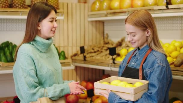 Mooie jonge boer dame in de groentewinkel hebben een gesprek met de klant een mooie dame de boer toont de oogst van citroen fruit aan de klant — Stockvideo