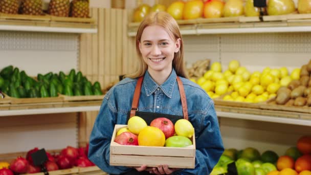 Koncepcja żywności ekologicznej w warzywniaku piękny z dużym uśmiechem rolnik pani pozowanie przed aparatem trzymając klatkę piersiową pełną owoców — Wideo stockowe