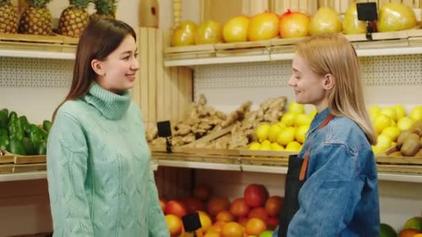 En la tienda de verduras orgánicas en frente de la cámara carismática cliente dama tener una conversación con la vendedora al final de la vendedora dando la bolsa eco comercial llena de maduro y orgánico — Vídeo de stock