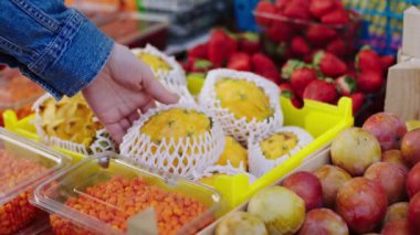 Ekolojik sebze dükkanındaki kameranın önünde müşteri kutudan bir tane sarı egzotik meyve alıyor.