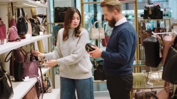 Vendedor feliz y atractivo ayudando a la señora cliente a elegir una de las bolsas del concepto de tienda de accesorios de pequeña empresa y empresario — Vídeos de Stock