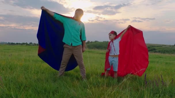 Eccitato carino piccolo ragazzo e suo padre che giocano insieme in un supereroi indossano tuta supereroi in mezzo alla natura al tramonto si godono il tempo insieme — Video Stock