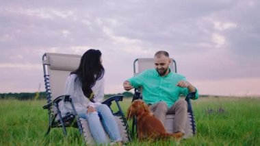 Heyecanlı adam ve sevimli köpeği eşiyle birlikte yeşil tarlanın ortasında sandalyelerde otururken doğanın heyecanını ve mutluluğunu hissediyorlar.