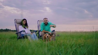 Heyecanlı, gülümseyen, çok karizmatik bir çift. Pikniğin tadını çıkarın. Muhteşem doğa mekanında, manzara, şirin, küçük bir İngiliz cocker spanyel köpeğiyle oynuyor.