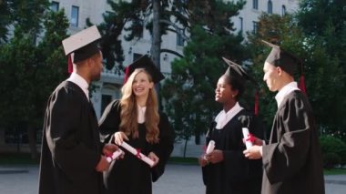 Üniversite bahçesinden mezun olan bir grup öğrenci ellerinde diplomalarıyla birlikte mutlu bir şekilde gülümseyerek ve heyecanlı bir şekilde tartıştılar.