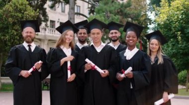 Çok ırklı öğrencilerden oluşan bir grup öğrencinin önünde ellerinde diplomalarla mezuniyet şapkalarını takmış kameraya bakarken heyecanlanıyor.
