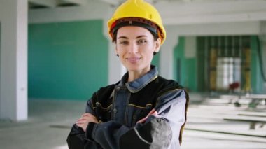 Güneşli bir günde güvenlik kaskı ve teçhizatı ile inşaat alanında kameranın önünde poz veren karizmatik bir gülümsemesi olan güzel mühendis kadın. ARRI Alexa Mini 'de çekilen.