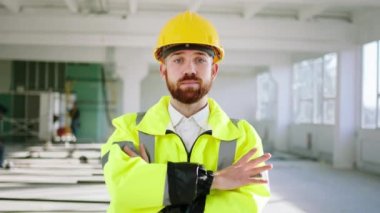 Kameranın önünde el ele tutuşarak poz veren yakışıklı inşaat işçisi inşaat alanında güvenlik kaskı ve ekipman takıyor.