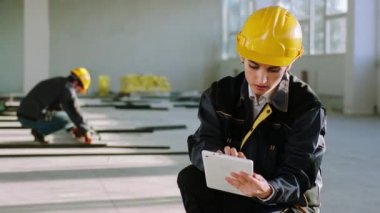 Modern, büyük bir inşaat alanında, dijital tablet kullanan koruyucu ekipmanlı bir mühendis kadın inşaat malzemelerinin kodlarını yazarak online dükkandan sipariş veriyor.