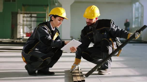 有大型空间建筑建筑工人的建筑工地，他们分析建筑材料并一起讨论戴防护设备的问题 — 图库视频影像