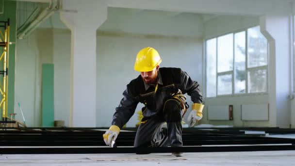 Divertente tempo al lavoro in cantiere giovane ragazzo in uniforme speciale e casco di sicurezza che utilizza un pennello per dipingere i materiali da costruzione e ballare durante l'ascolto di musica dal wireless — Video Stock