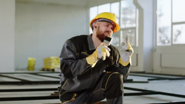建筑工地上迷人而令人兴奋的建筑工人，带着安全帽和安全设备，用画笔粉刷建筑材料 — 图库视频影像
