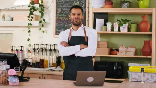 In een leuke coffeeshop een zwarte charismatische man barista typen iets op de laptop dan kijken naar de camera en poseren hij lachend schattig — Stockvideo