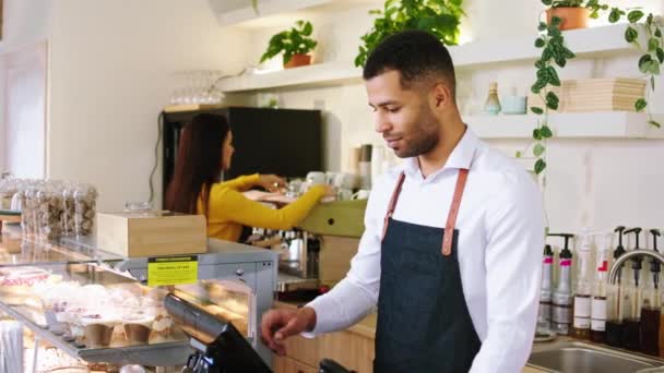 V moderní kavárně před kamerou Afro Američan muž s roztomilým úsměvem pózuje před kamerou křížení rukou, zatímco jiné věci žena pracuje na pozadí — Stock video