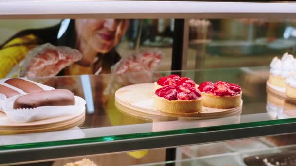 Nahaufnahme mit der Kamera Verkäuferin nehmen einige Desserts aus der Vitrine Kühlschrank zu verkaufen, sie lächelt groß und trägt Schutzmaske in der Pandemie des Coronavirus — Stockvideo