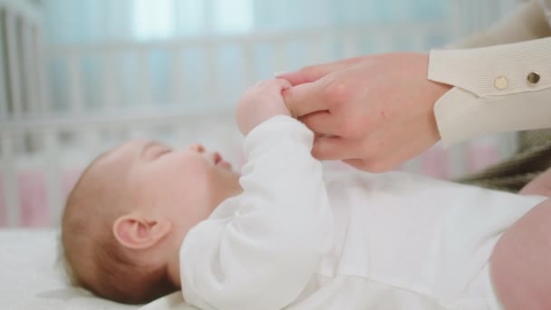 Vor der Kamera fühlt sich das hübsche Baby zusammen mit seiner Mutter wohl, hält die Hände zusammen und legt sich aufs Bett — Stockvideo