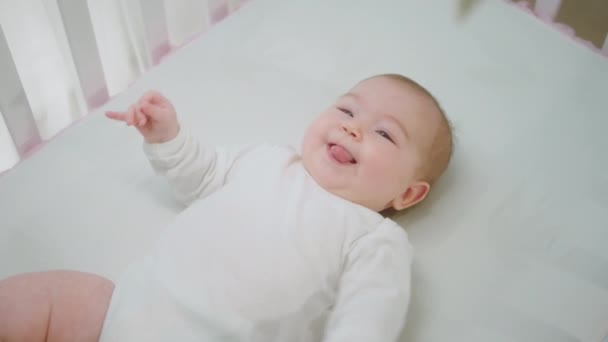 Λήψη βίντεο από το παραπάνω κοριτσάκι πολύ χαριτωμένο ξαπλωμένη στο κρεβατάκι του μωρού της και παίζοντας με τα παιχνίδια που κινούνται από τα χέρια και τα πόδια — Αρχείο Βίντεο