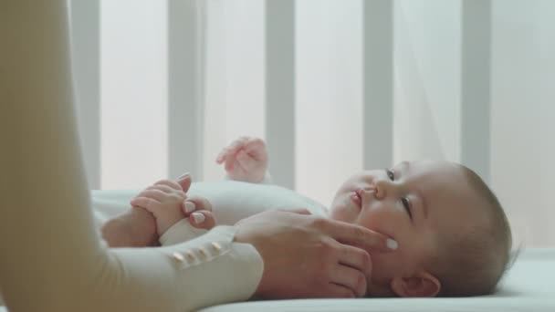 Close up to the camera cute baby girl playing with her mother young mother 's hands touching the baby face while baby are in the baby cot — стоковое видео