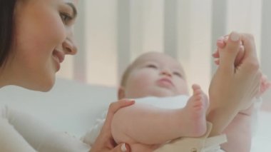 Çekici genç annenin portresi. Günlük rutinini yapıyor. Bebeğin bacaklarını dikkatlice tutuyor.
