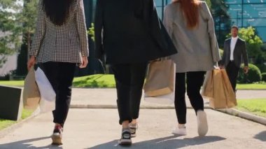 İş yerindeki çok kültürlü iş arkadaşları ellerinde alışveriş torbalarıyla sokakta yürürken arkalarından video çekiyorlar.