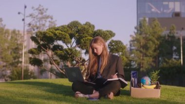 Central Modern Park 'taki güzel iş kadını çalışmak için dizüstü bilgisayar kullanıyor ofis eşyalarını bir kutuya koyup işine konsantre oluyor. Arri Alexa Mini.