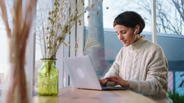 Sorrindo mulher grande com um rosto bonito trabalhando on-line em seu laptop digitando algo enquanto sentado em uma cafeteria moderna com grande vista panorâmica — Vídeo de Stock