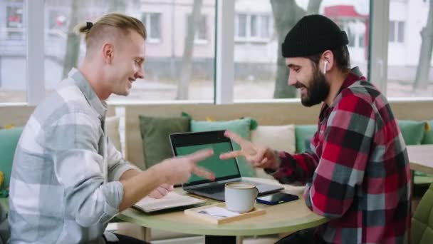 Два хороших друга делают проект колледжа вместе они играют в камень бумаги ножницы, чтобы знать, кто победит в кафе они используют ноутбук для изучения — стоковое видео