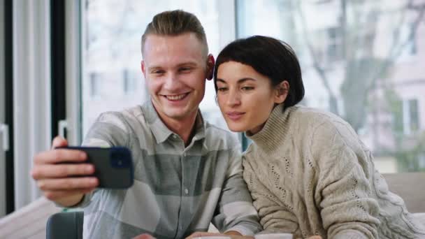 Dans une journée ensoleillée dans le café charismatique beau couple faire quelques selfies à partir du smartphone ils se serrant dans leurs bras et souriant mignon. 4k — Video