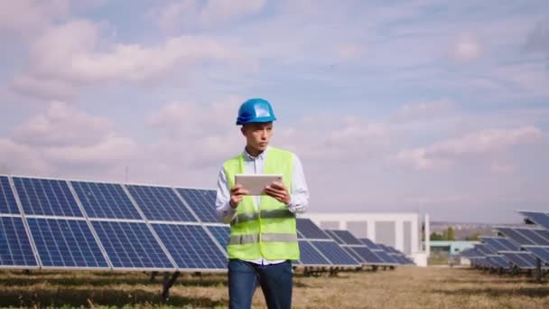На инновационной электростанции азиатский инженер-эколог, работающий с цифровым планшетом, он контролирует фотоэлектрические батареи от беспроводной сети в парке солнечных батарей — стоковое видео