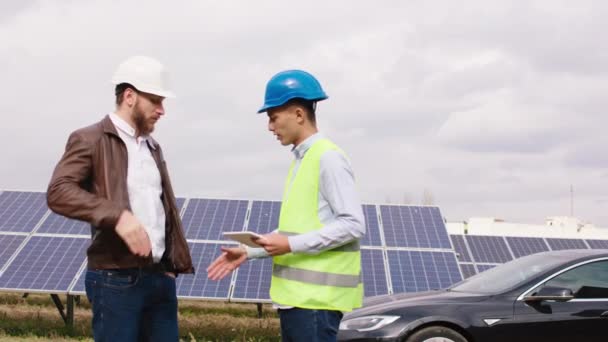 Un giovane lavoratore ecologico e ingegnere industriale nella moderna fattoria dei pannelli solari terminano la discussione e si stringono la mano alla fine accanto all'auto elettrica. — Video Stock