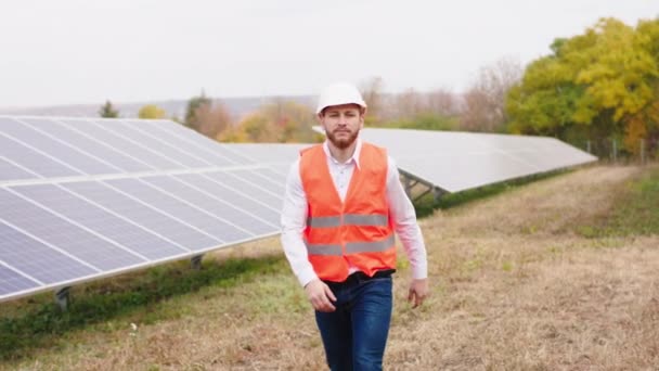 Fogalma ökológiai innováció és zöld energia séta előtt a kamera ökológiai mérnök, majd megáll, és pózol keresztbe kezét mosolyogva nagy a napelemek farm — Stock videók