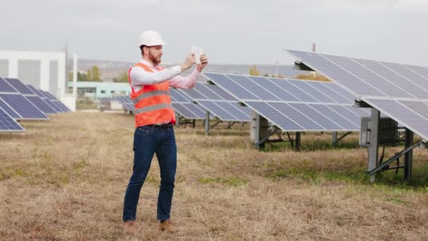 太阳能电池板的生态创新概念农场富有魅力的工业机械师，戴着安全帽，用数字平板控制无线光伏电池 — 图库视频影像