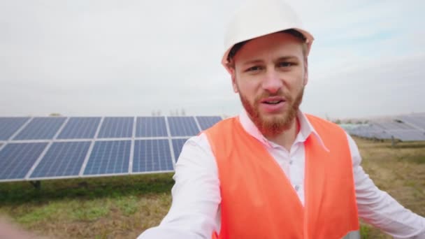 Промислово-механічний чоловік на сонячній електростанції бере селфі-відео він захоплює поле сонячних панелей він говорить про деякі проблеми концепції зеленої енергії — стокове відео