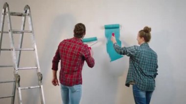 Genç ve mutlu bir çiftin duvar fırçasını kullanarak yatak odasının duvarlarını boyama zamanı. Birlikte anın tadını çıkarıyorlar.