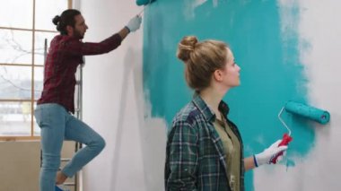 Güzel bayan kocasıyla birlikte oturma odasında duvar fırçası silindirini kullanarak duvarları boyuyor.