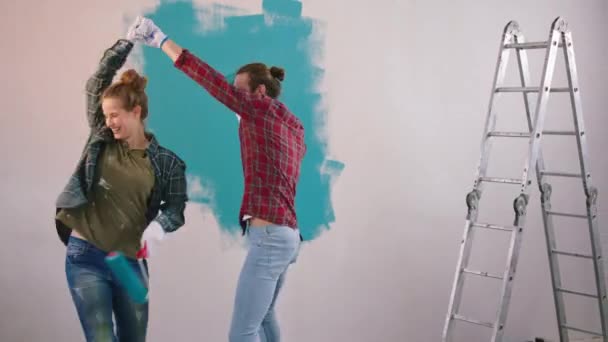 Bardzo szczęśliwa i charyzmatyczna para przytulająca się podczas malowania ścian w domu i tańcząca razem trzymając pędzle ścienne w rękach — Wideo stockowe