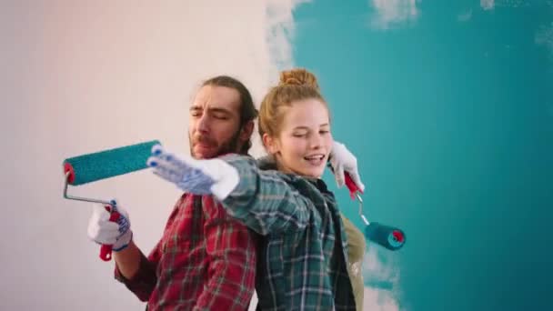 Aantrekkelijk echtpaar Kaukasisch kijkend voor de camera dansen opgewonden samen thuis terwijl het schilderen van de muren in de woonkamer. 4k — Stockvideo