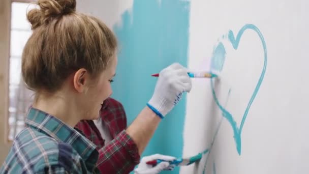Beau couple excité ensemble peinture murs à la maison dans le salon, ils font un grand cœur et la peinture avec un petit pinceau ensemble et souriant grand — Video