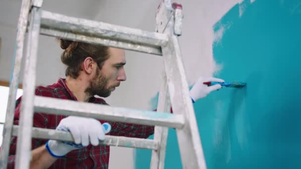 Concentré homme charismatique de travail à l'aide d'un petit pinceau pour peindre parfait les murs qu'il debout sur l'échelle — Video